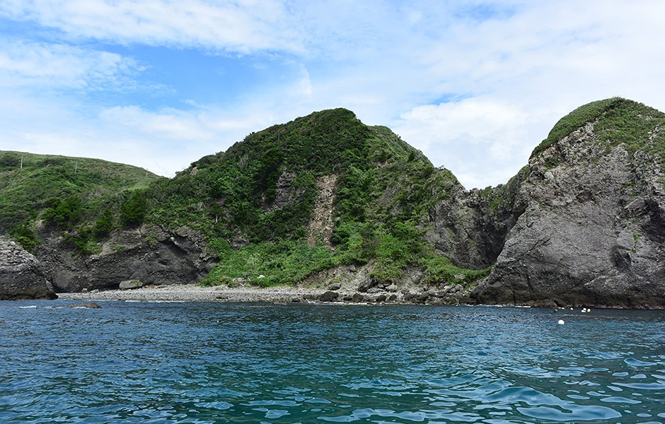   沖から見たヒリゾ浜。100メートルほどのゴロタの浜の背後は断崖がそびえ、陸からはアプローチができません。安全のため、白いブイで遊泳区域は区切られています。