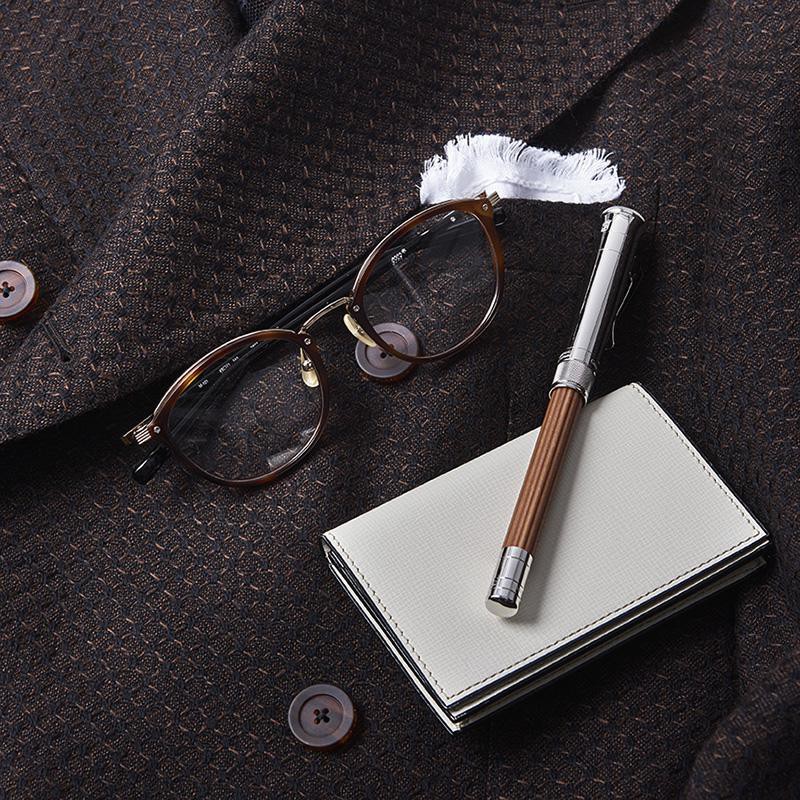 ジャケットのブラウンを基調に決めたら、小物は旬な茶系で揃えるのが吉。いたるパーツがリッチでコクまろなフォーナインズの「M-101」は、まさにその大代表です。全てが同系色では蒙昧な印象に陥りかねないため、コントラスト付けのために差したホワイトチーフを拾い、名刺入れにはヴァレクストラの白をチョイス。筆記具はファーバーカステルの鉛筆一筋、こだわりの強い嗜好性が垣間見られます。メガネは上と同じ、ペンシル4万5000円/ファーバーカステル(DKSHジャパン)、名刺入れ3万8000円/ヴァレクストラ(ヴァレクストラ・ジャパン)