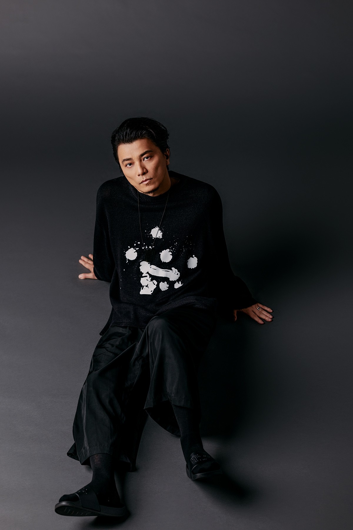 この“黒”は、ただの黒にあらず。異なる質感の“黒”を、緻密に、大胆に重ねて。そこに宿るのは品と艶、そしてストリートの余韻。タックショートパンツ4万6200円、ドッグタグ6798円(*6/21より受注開始予定)、ソックス4620円、シャワーサンダル9988円／KREVA×ALMOSTBLACK、ニット4万6200円／ALMOST BLACK、リング／私物